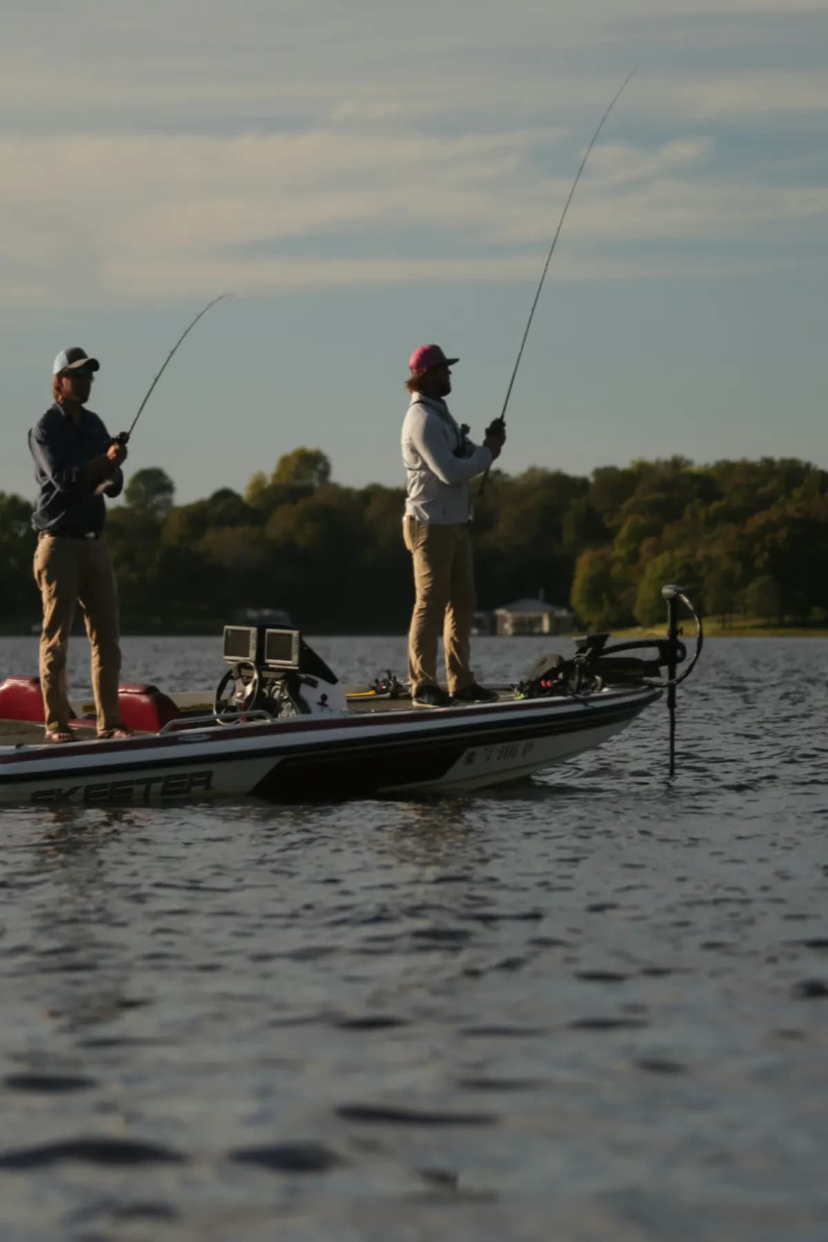 Two anglers casting from a bass boat in the evening